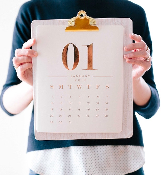 A woman holding up a clipboard with a calendar in front of her chest. Original public domain image from Wikimedia Commons